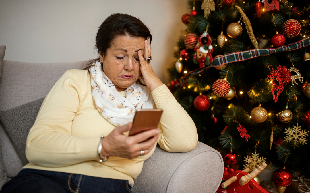woman sat on chair next to a Christmas tree looking at her phone