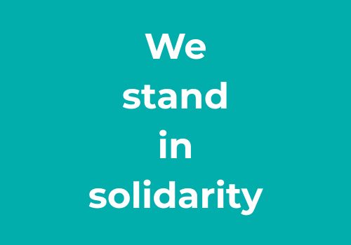 Blue background, white writing stating 'we stand in solidarity'