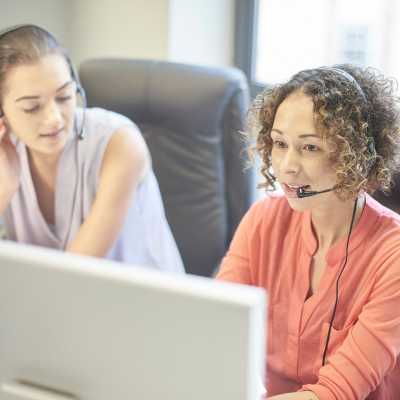 two women with headphones sat at laptop